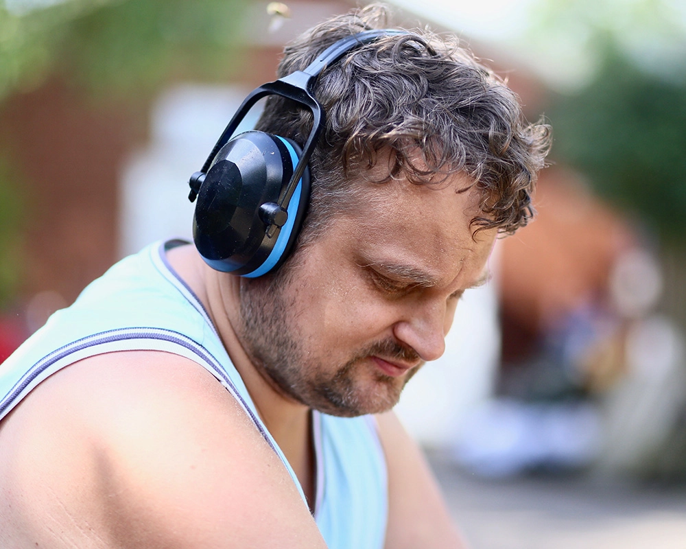 Kopf mit Hörschutzkopfhörern und Oberkörper eines Mitarbeitenden der Tagesstätte Bauhof.