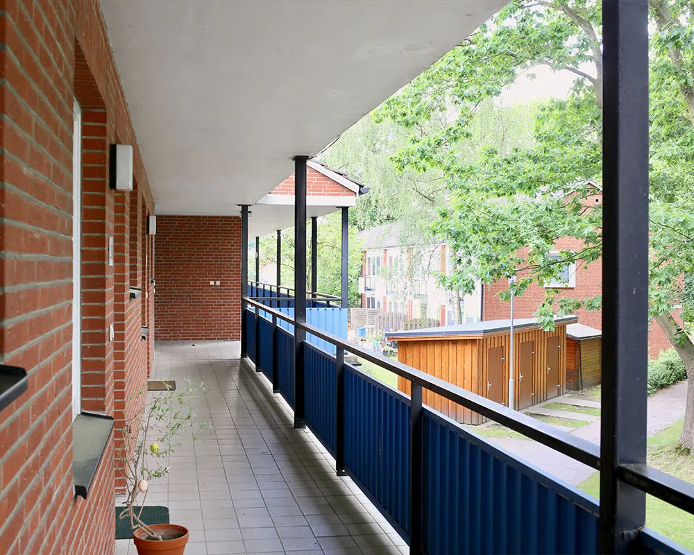 Ein langer, überdachter Außenflur mit Geländer erstreckt sich entlang einer Backsteinfassade.