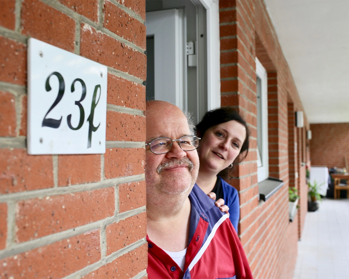 Das Bild zeigt den Eingangsbereich eines Backsteingebäudes. Zwei Personen stehen in der geöffneten Tür des ambulant unterstützes wohnen.