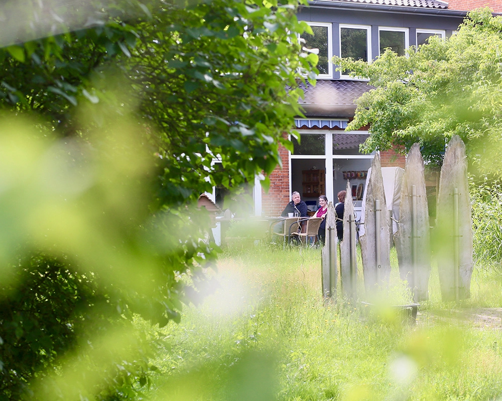 Drei Bewohner des Betreuten Wohnens sitzen im Garten an einem Tisch vor der Terrassentür