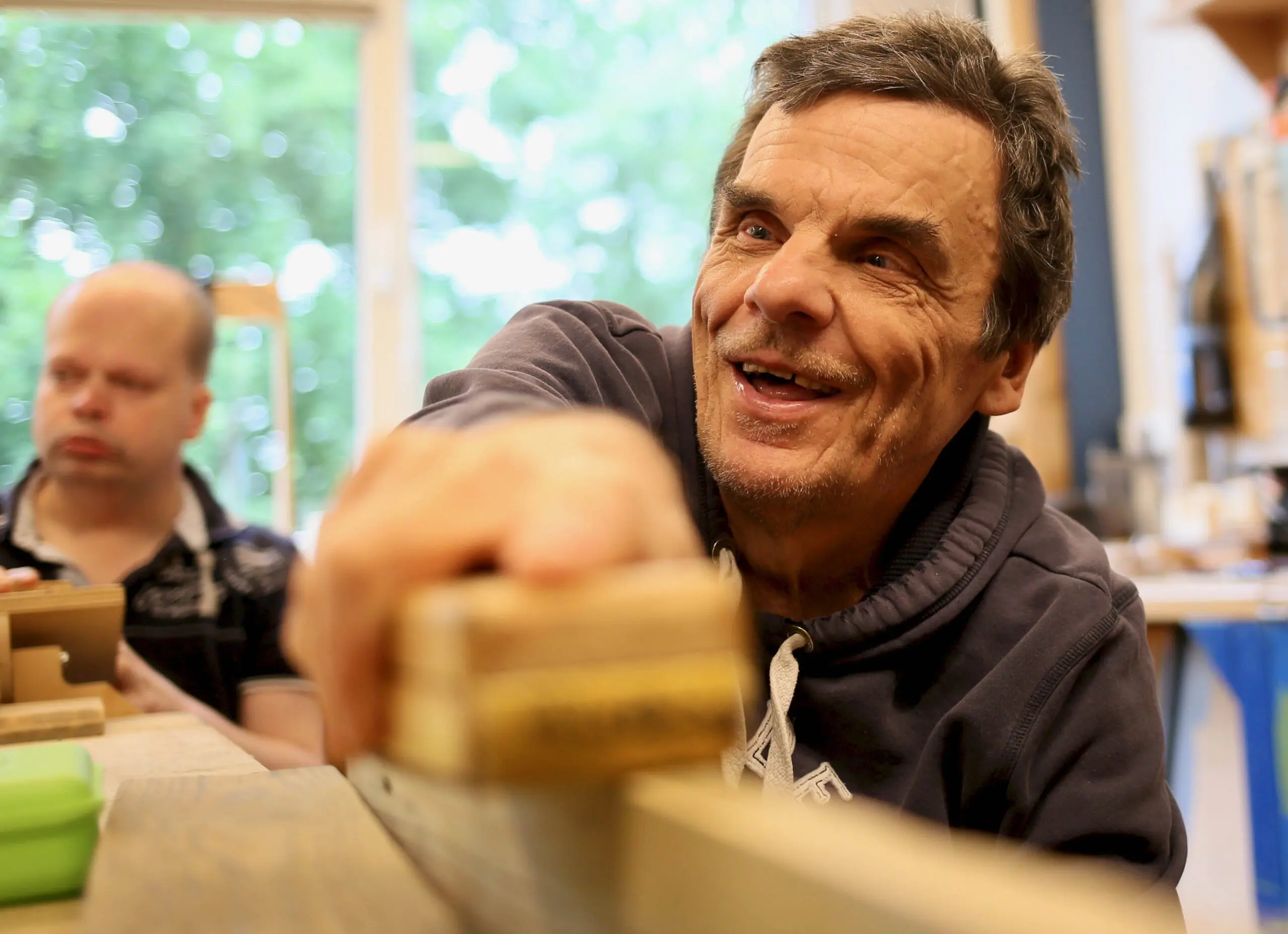 Ein Bewohner arbeitet in einer Werkstatt mit einem Holzwerkzeug an einem Werkstück.